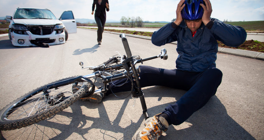 Road accident. Car and bicycle Bicyclists injured in a car accident lying down on the road and holding his head with helmet. A person who is driving car running to helps to injured man
